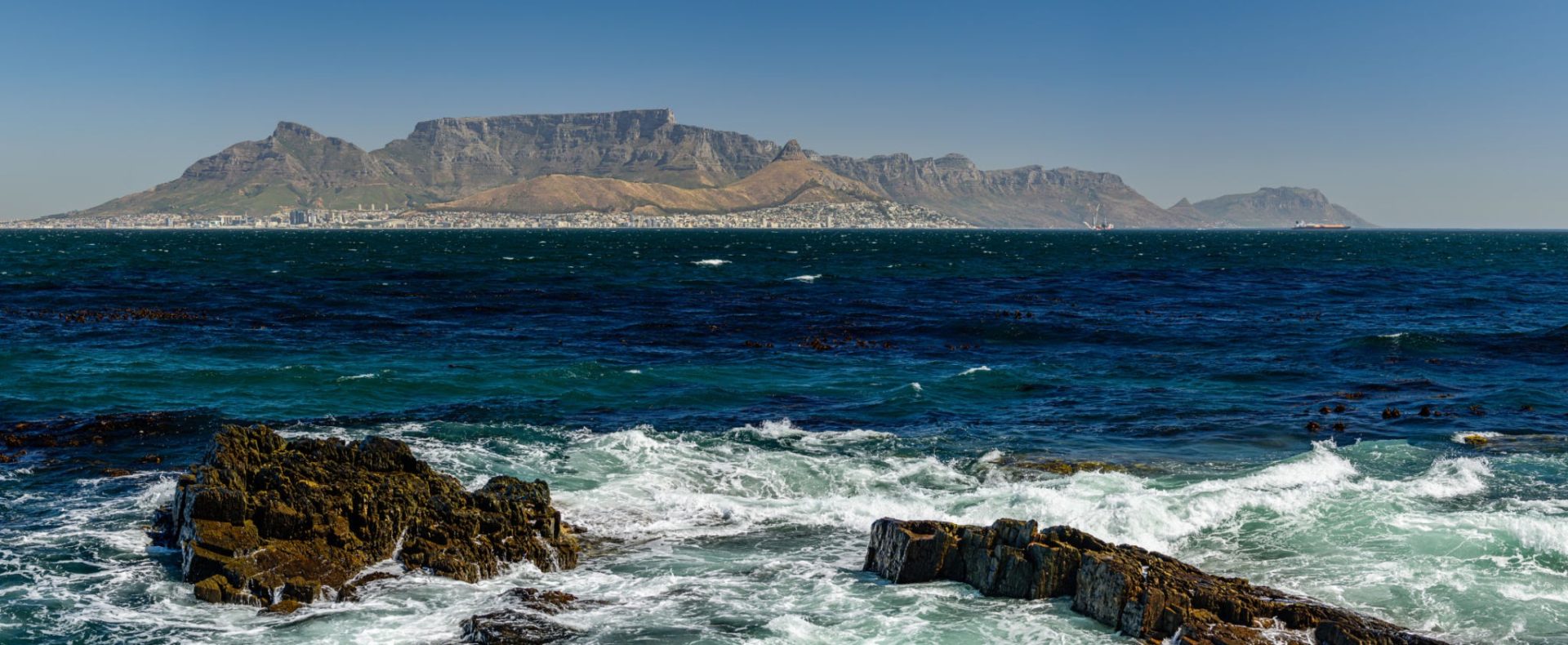 Table mountain in Cape Town from the distant Robben Island. Rocky cliffs in the foreground.